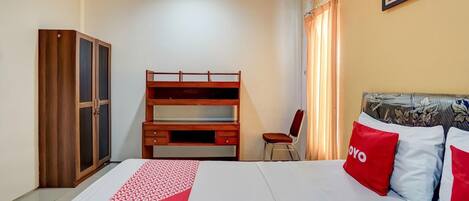 A hotel room with a bunk bed, a wardrobe, a desk, a chair, and a bed with red and white pillows.