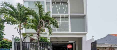A modern two-story building with a gated entrance, a sign indicating a residential complex, and a clear sky.