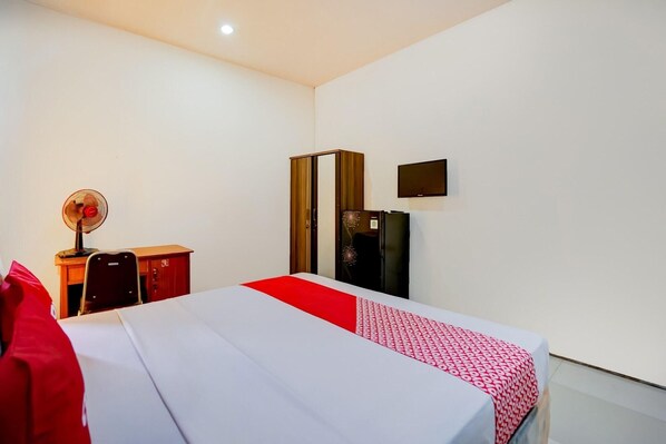 A hotel room with a bed, a desk, a chair, a wardrobe, a refrigerator, and a television.