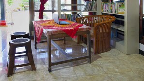 A room with a wooden chair, a small table, a bookshelf, and a window with curtains. - OYO Homes 91134 Desa Wisata Tebing Lingga (Nglebo)