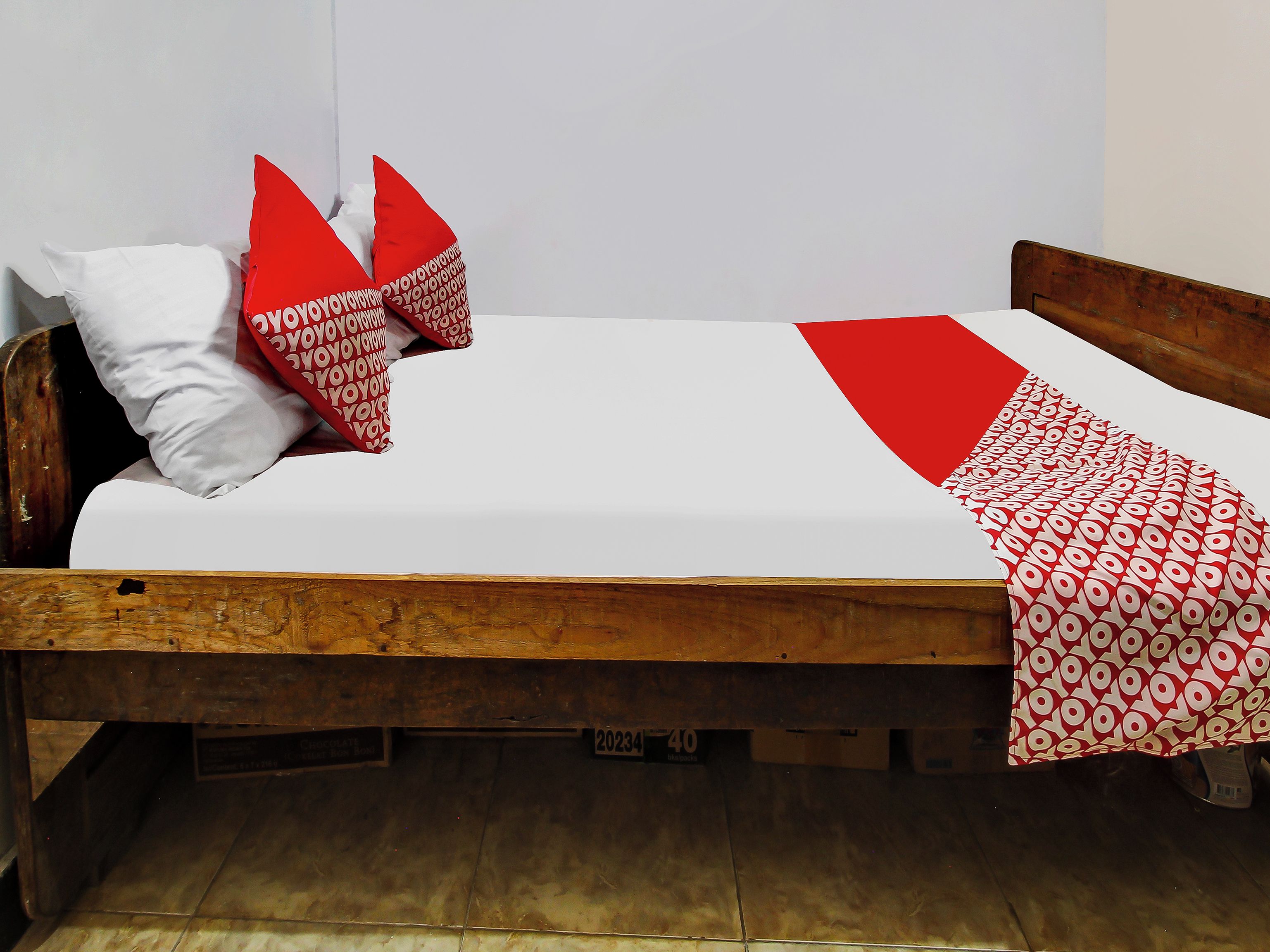 A single bed with a wooden frame, white bedding, and red and white patterned pillows.