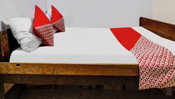 A single bed with a wooden frame, white bedding, and red and white patterned pillows.