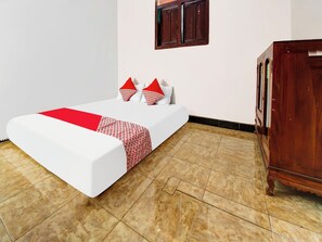 A neatly arranged bedroom with a bed, pillows, a wooden cabinet, and a tiled floor.