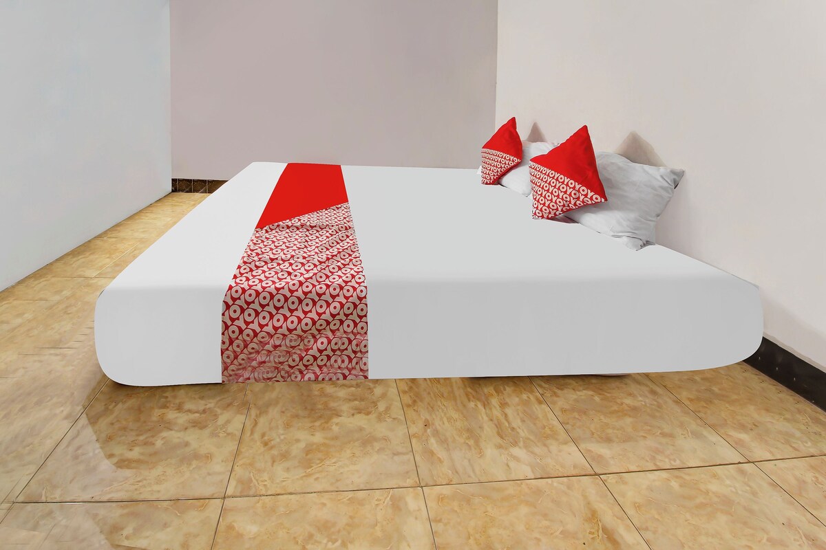 A neatly made bed with a white mattress and red patterned bedspread.