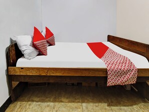 A single bed with a wooden frame, white bedding, and red and white patterned pillows.