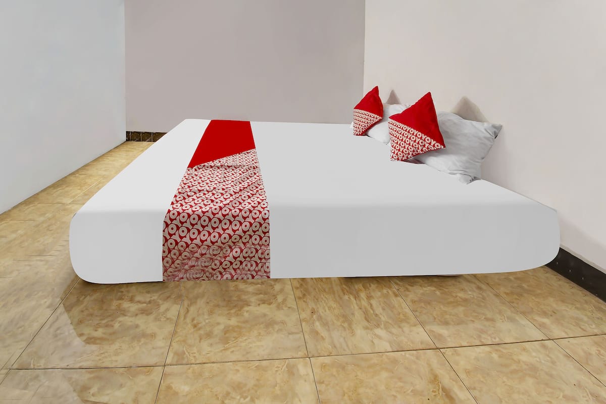 Un lit bien fait, avec un matelas blanc et une couvre-lit rouge à motifs.