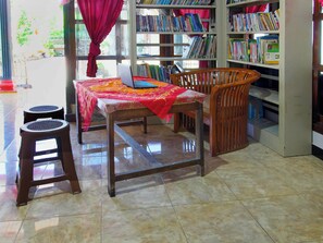 A room with a wooden chair, a small table, a bookshelf, and a window with curtains. - OYO Homes 91134 Desa Wisata Tebing Lingga (Nglebo)