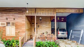 A wooden exterior with a covered porch, a car parked inside, and a ladder leaning against the wall. - OYO Homes 91067 Desa Wisata Santanamekar (Cisayong)