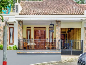 Une maison avec un toit en tuiles, une véranda dotée d’une balustrade et une voiture garée devant.