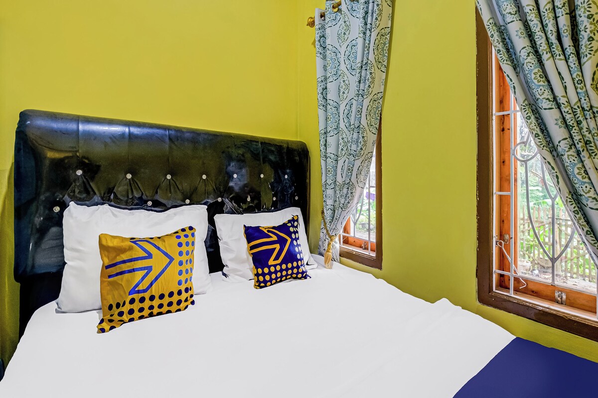 A bed with white bedding, two pillows with geometric patterns, a dark headboard, and a window with patterned curtains.