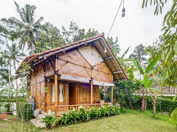 Ein rustikales Holzhaus mit Strohdach, umgeben von üppigem Grün und einem kleinen Teich.
