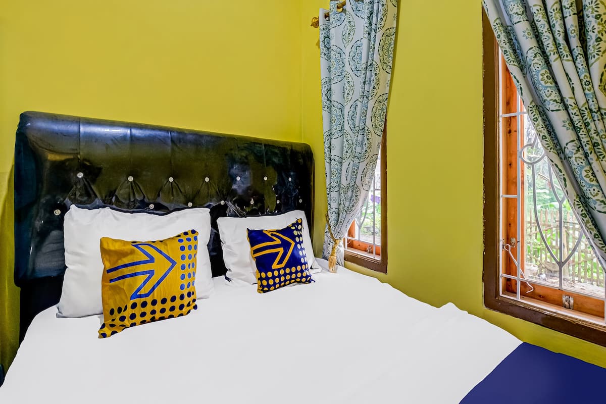 A bed with white bedding, two pillows with geometric patterns, a dark headboard, and a window with patterned curtains.