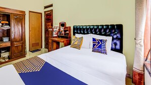 A hotel room with a bed, a wooden wardrobe, a desk with a mirror, and a window with curtains.