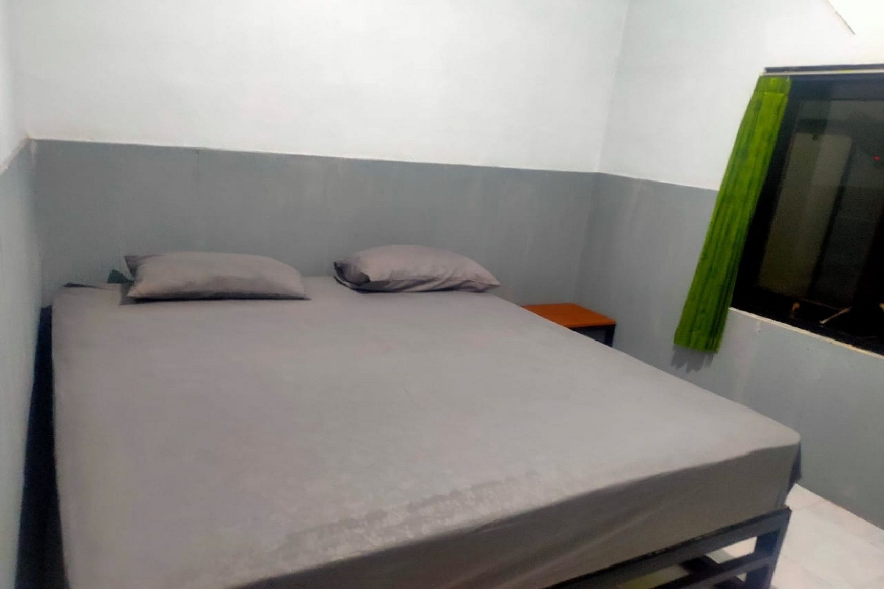 A single bed with a grey mattress and two pillows in a room with light blue walls.