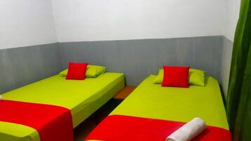 A room with two single beds, each with a red pillow and a green bedspread.