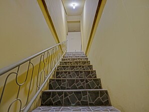 Una escalera con baldosas estampadas y barandillas de metal, que conduce a una plataforma con una lámpara en el techo.
