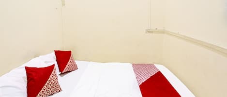 A bed with white and red bedding, two pillows, and a plain wall.