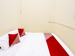 A bed with a white and red bedspread, two red pillows with a white pattern, and a plain wall with a light switch.