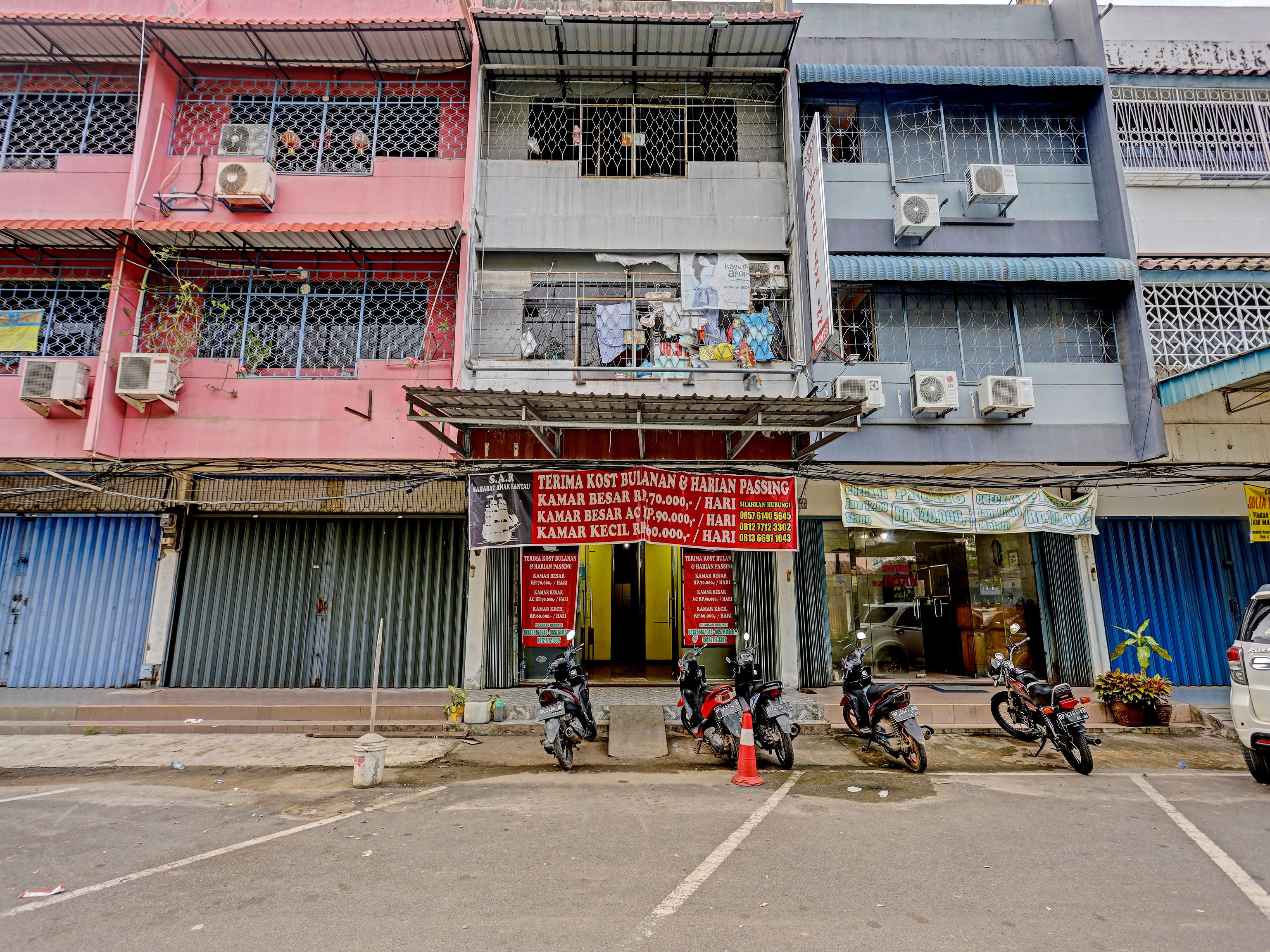 A multi-story building with air conditioning units, a storefront with a sign, and motorcycles parked in front.