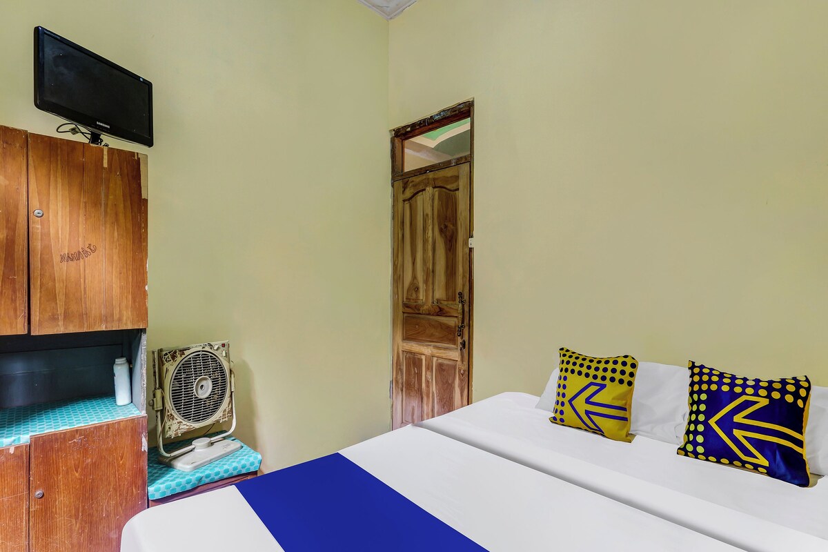 A bedroom with a bed, wooden wardrobe, a television, and a fan.