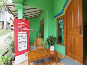 Un bâtiment écologique avec une porte en bois, une enseigne rouge, une chaise en osier, une table en bois et une plante en pot.
