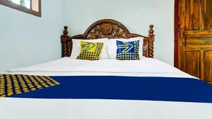 Ein Bett mit weißblauer Bettdecke, zwei Kissen mit gelbblauen Mustern und einem Holz-Kopfteil.