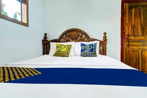 A bed with a white and blue bedspread, two pillows with yellow and blue patterns, and a wooden headboard. - OYO 91242 Desa Wisata Cibuntu Kuningan Syariah (Mandirancan)