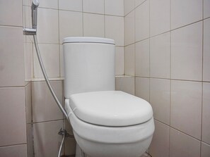 Des toilettes blanches dans une salle de bain aux murs carrelés, avec une pomme de douche fixée au mur.