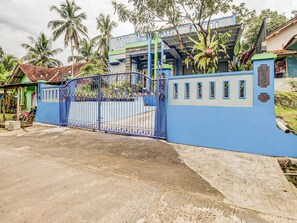 Un lotissement résidentiel fermé, délimité par un mur bleu, une porte en métal et une maison avec un toit en tuiles.