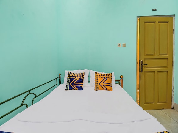 A bed with white bedding, two pillows with geometric patterns, a green metal headboard, and a wooden door.