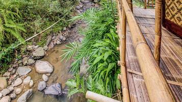 Un pont de bambou enjambant un ruisseau, avec des rochers et de la végétation.