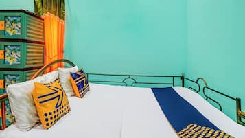 Een bed met een wit- en blauw gestreept dekbedovertrek, twee kussens met gele en blauwe patronen, en een groen metalen frame.