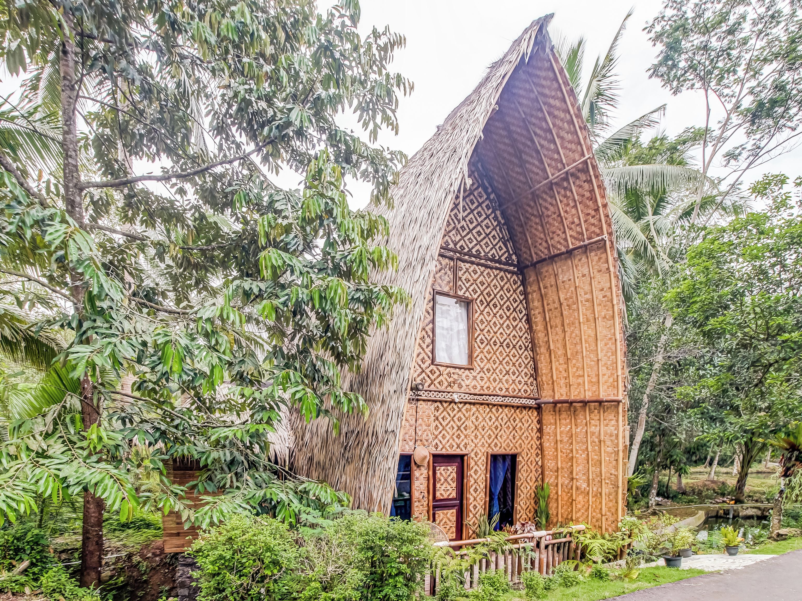 A unique, triangular-shaped building with a patterned facade, surrounded by lush greenery and a small water feature.