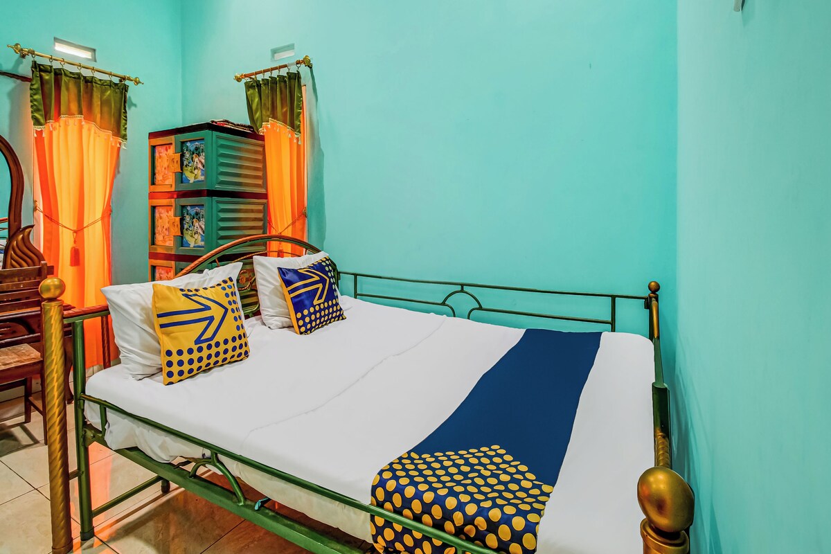 Une chambre avec un lit simple, un cadre en métal, un matelas blanc et des coussins à motifs.