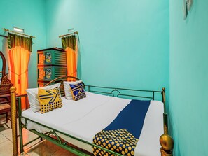 Une chambre avec un lit simple, un cadre en métal, un matelas blanc et des coussins à motifs.
