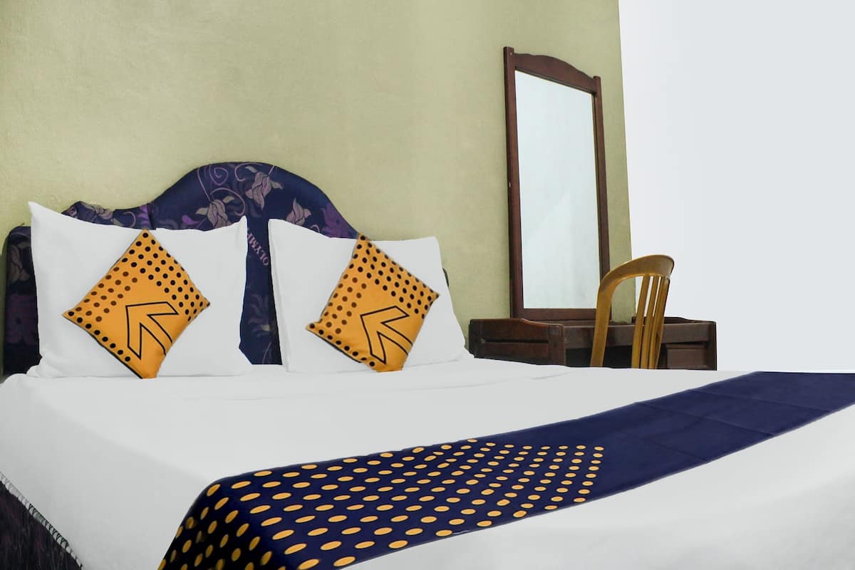 Un lit bien fait, recouvert d’une couverture à pois bleus et jaunes, avec deux oreillers blancs à pois jaunes, et une chaise en bois placée à côté du lit.