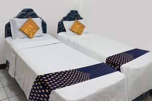 Zwei Einzelbetten mit weißer Bettwäsche und blauen Kopfteilen, jeweils mit einem gelben Kopfkissen mit schwarzem Pfeilmuster.