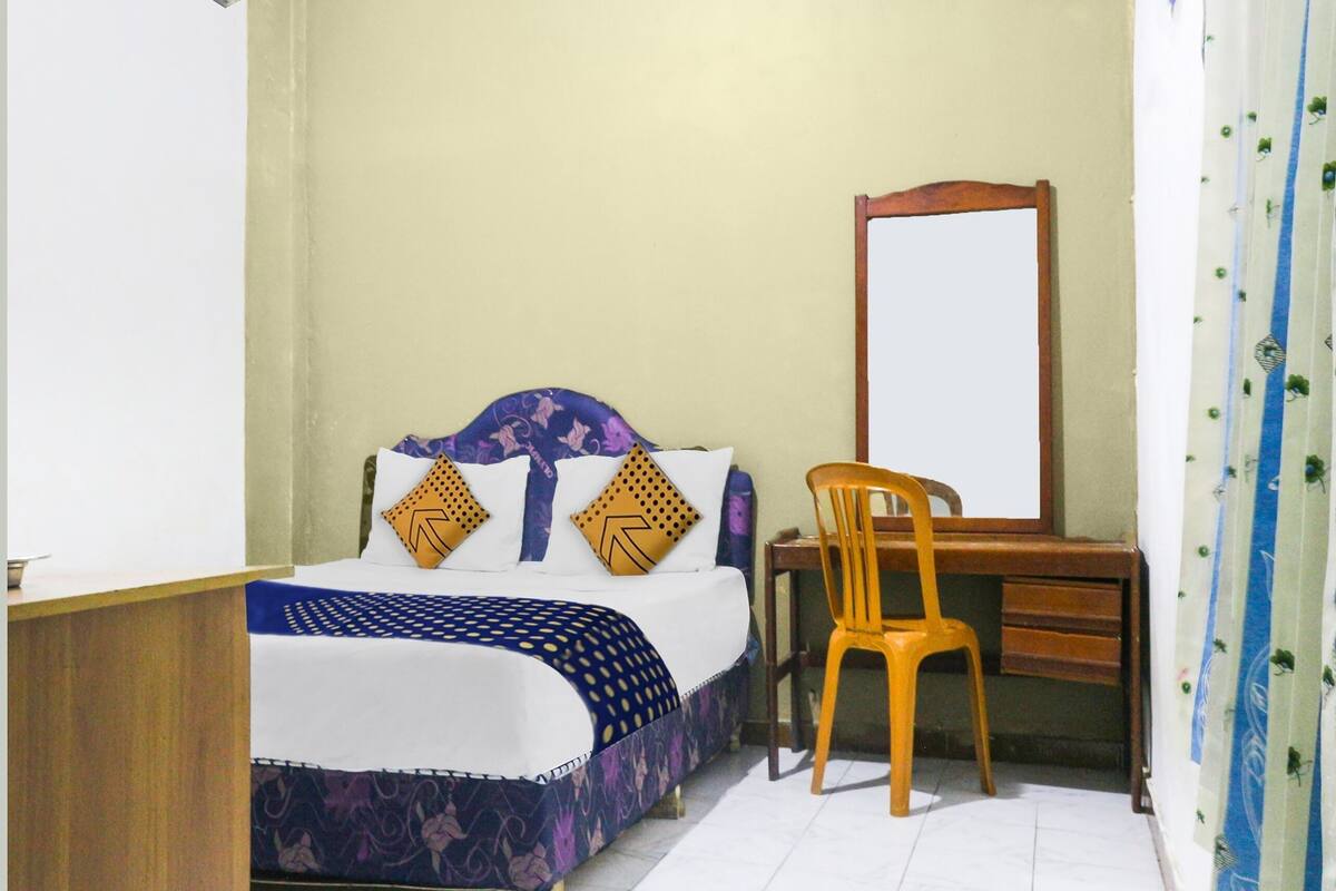 Une chambre à coucher avec un lit, une chaise en bois, un bureau et un miroir.