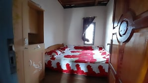 Una habitación con una cama, un armario de madera, un ventanal con cortinas y una puerta con pomo redondo.