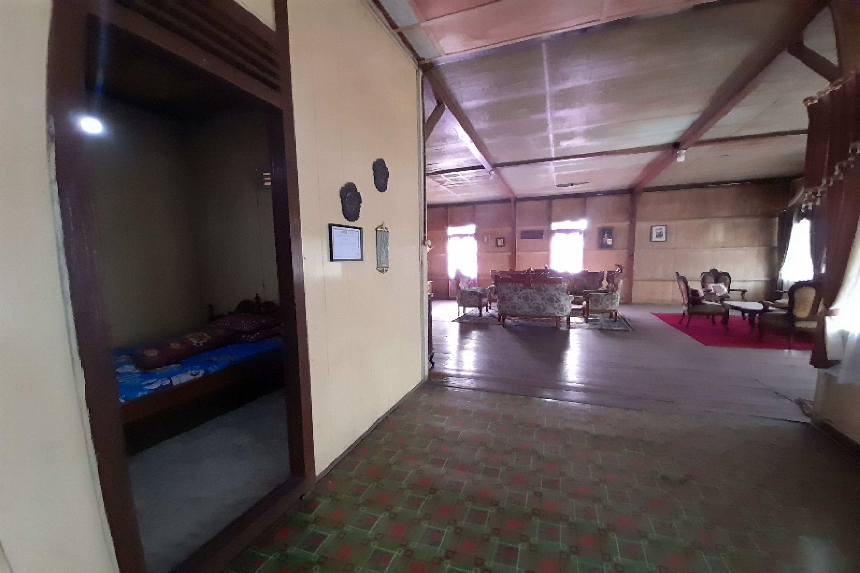A spacious room with a high ceiling, a bed with a blue mattress, a wooden door, and a red carpet.