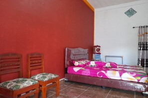 A bedroom with a bed, two wooden chairs, a red wall, and a tiled floor. - OYO Homes 91248 Desa Wisata Banding Agung Danau Ra (Banding Agung)