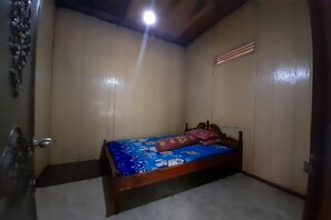 A small, single-bed room with a wooden headboard, a blue bedspread with cartoon characters, and a wooden door with a metal handle. - OYO Homes 91248 Desa Wisata Banding Agung Danau Ra (Banding Agung)