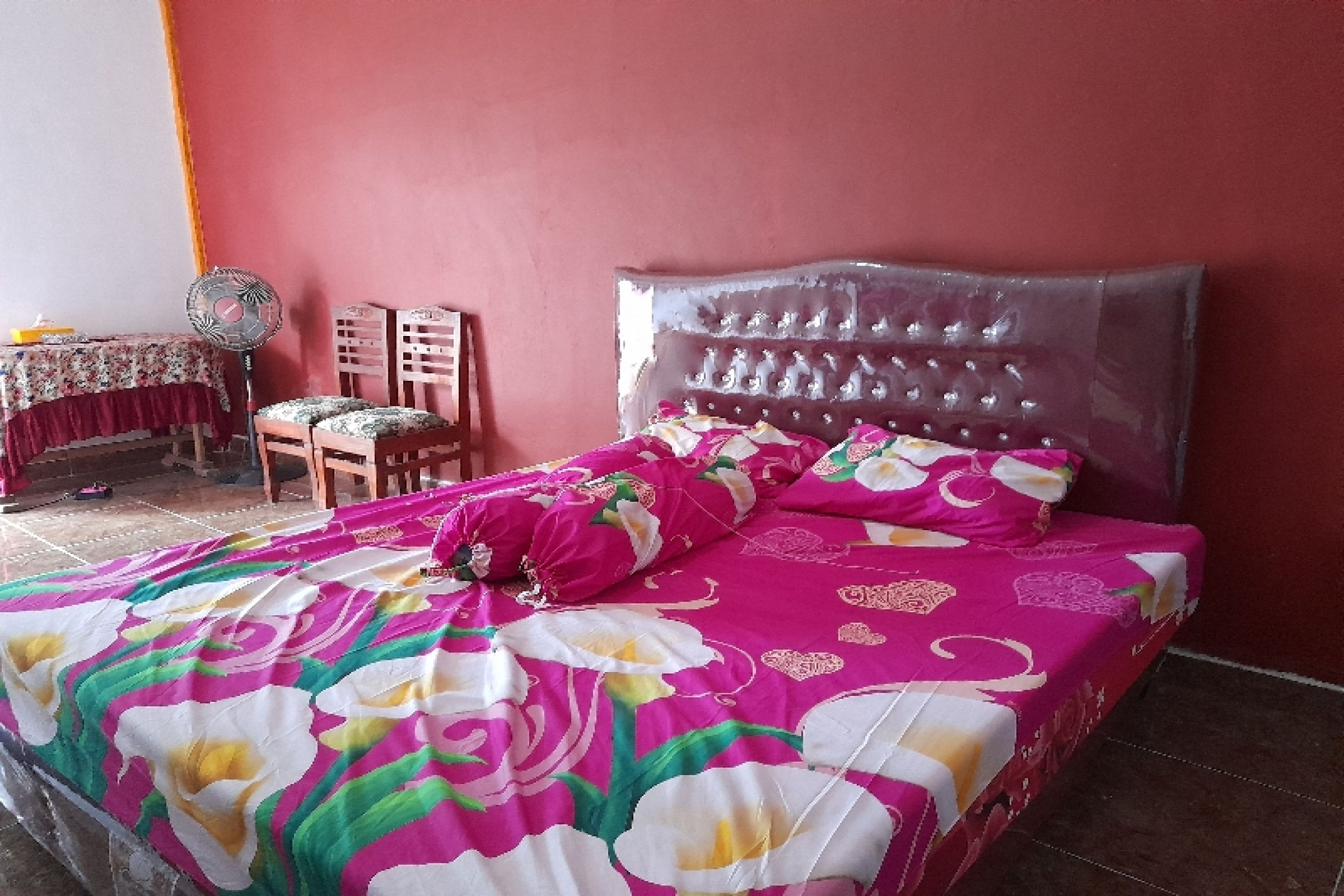 A bedroom with a bed, a chair, a table, and a fan.