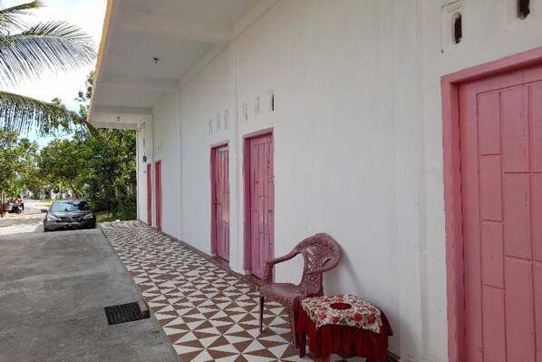 Un edificio con paseo de baldosas, puertas rosadas y un coche aparcado.