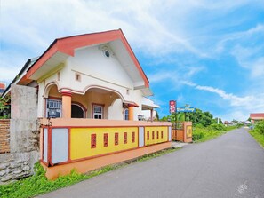 A two-story building with a red roof and a yellow facade, featuring a gated entrance and a clear sky in the background.
