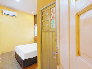 Quarto com cama, porta com placa indicativa CSF e unidade de ar condicionado na parede.
