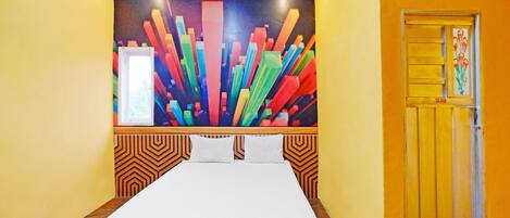 A hotel room with a bed, a colorful abstract wall art, a door with a floral design, and a patterned wall.