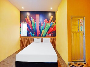 A hotel room with a bed, a colorful abstract wall art, a door with a floral design, and a patterned wall.