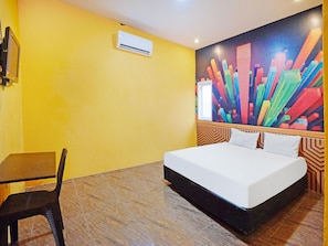 A hotel room with a bed, a desk, a chair, and a colorful abstract painting on the wall.