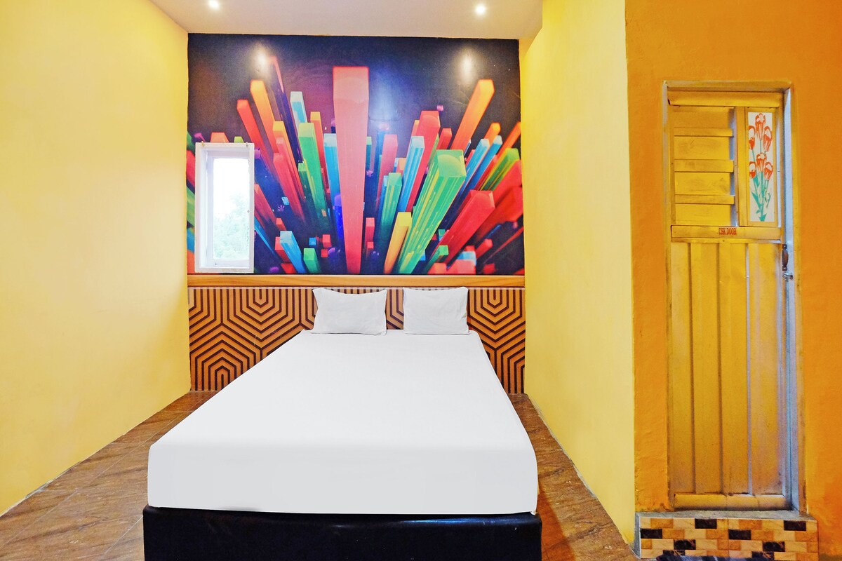 A hotel room with a bed, a colorful abstract painting on the wall, a door with a floral design, and a patterned wall.